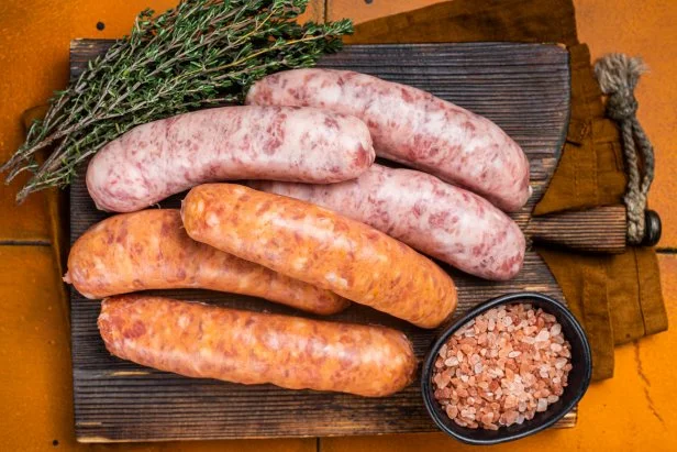Fresh Raw Bratwurst and Chorizo meat sausages on wooden board. Orange background. Top view.
