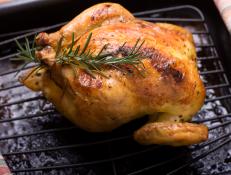 A roasted cornish game hen fresh out of the oven and garnished with a sprig of rosemary.