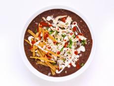 Slow cookers are perfect for turning dried beans into a creamy soup with almost no effort. Black beans are cooked with fire roasted tomatoes, poblano peppers and spices for a full flavor. For serving, rotisserie chicken is warmed with cumin and cilantro before topping the soup, then finished with crema, onion, tortilla strips and lime wedges.