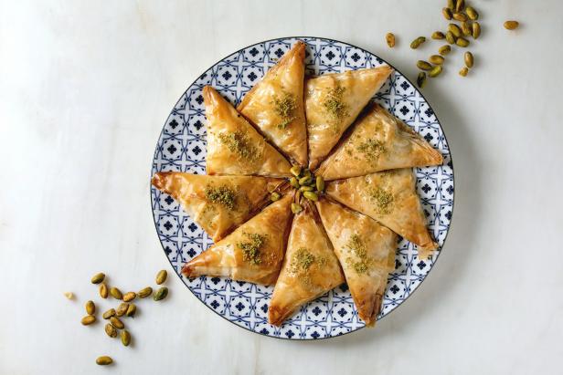 Homemade Turkish traditional dessert baklava with pistachio served on ornate plate over white marble background. Flat lay, space