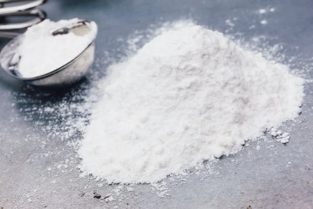 Heap of baking soda with measuring spoon on a metal baking tray.