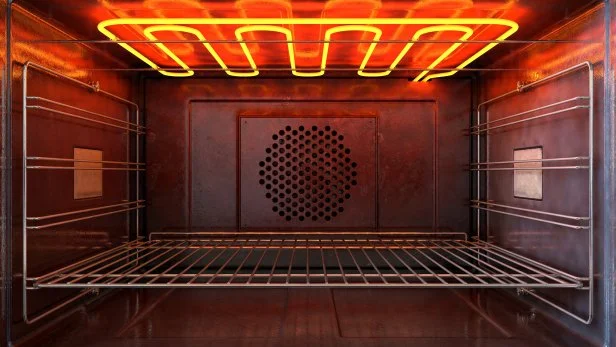 An upclose view through the front of the inside of an empty hot operational household oven with a glowing element and metal rack - 3D render