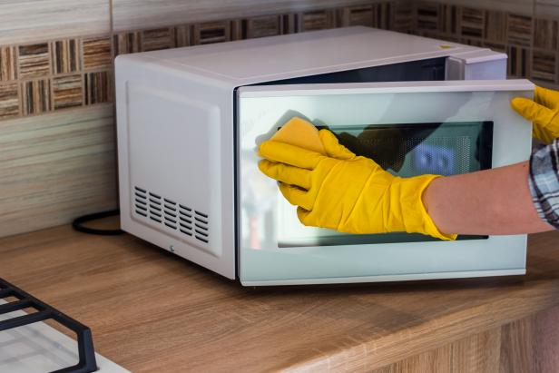 women's hands in yellow gloves washing sponge door microwave
