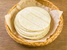Fresh white corn tortillas on a wood background.