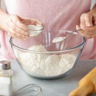 Women adds the baking powder into the glass bowl with flour. Step by step recipe of homemade mexican flatbread tortilla.