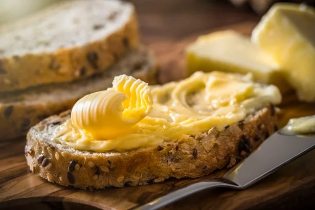 Front view of a slice of bread spread with butter with a butter curl on top