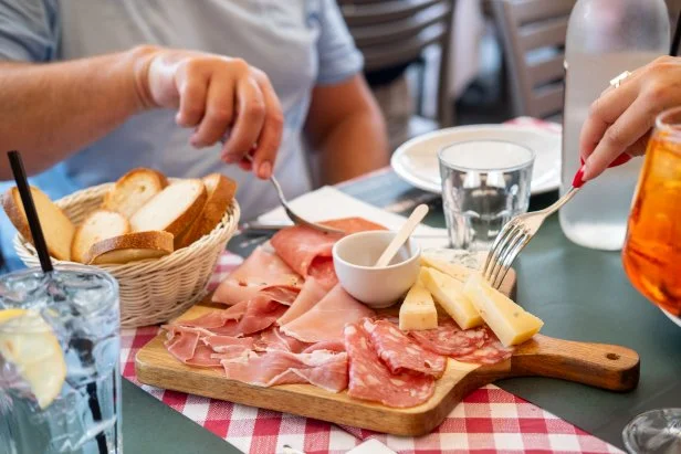 People in the restaurant eat Traditional antipasto in Italy, typical products of Rome prosciutto, Parma ham, mortadella and salami, parmesan and pecorino cheese and spritz