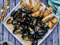 These tender grilled mussels are served with a buttery white wine-and-garlic sauce and plenty of crusty grilled bread to mop up the delicious juices. The high heat of grilling leaves mussels particularly plump, and it just might be one of the easiest ways to cook them: There&rsquo;s no need to pull out a big pot for steaming and cleanup is a breeze. We bumped up the sauce by using a whole head of garlic first softened in the microwave to cut the cooking time and then caramelized it right on the grill for natural sweetness and tons of umami. It&rsquo;s a rich, satisfying dish bursting with flavor.