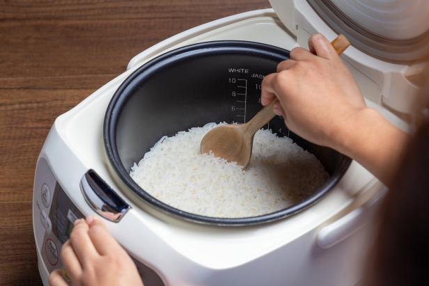 Woman hand is scooping jasmine rice cooking in electric rice cooker with steam. Thai Jasmine rice.