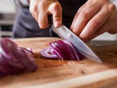 Cette photo reprÃ©sente une personne en train de couper des oignons rouges dans une cuisine.