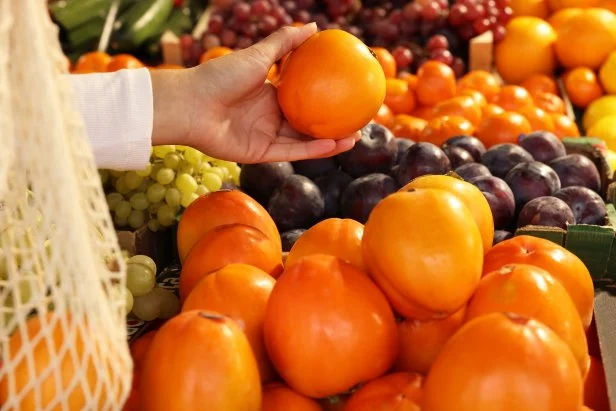 Woman picking fresh persimmon at market, closeup