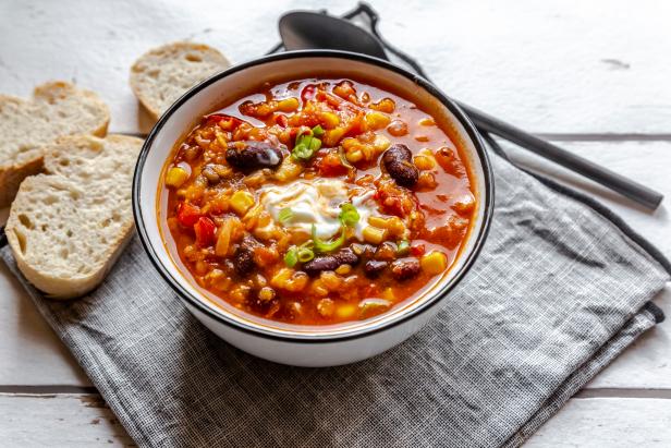 Linsenchili, Chili sin carne, vegetarisches Chili mit roten Linsen, Chilibohnen, Mais, Tomaten, Paprika, Lauchzwiebel und Joghurttopping, Baguette