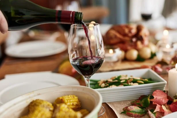 Red wine, hand and pour at Christmas feast or celebration holiday, event or festive season. Glass, alcohol or bottle closeup for drink at party table for lunch food, social gathering or vacation meal