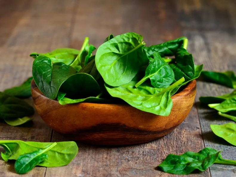 Spinach leaves in a wooden bowl on a wooden table.