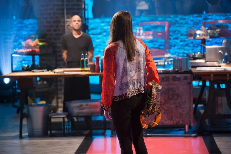 Sophie Flay holds a lobster behind her back, as seen on Food Networks Beat Bobby Flay, Season 5.