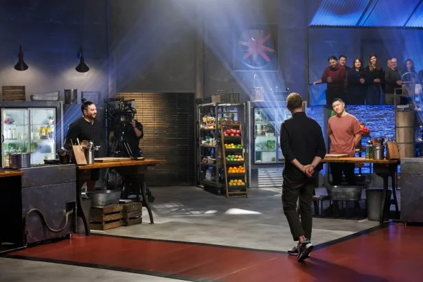Bobby Flay addresses contenders Logan Sandoval and Laurence Louie at their cooking stations before they begin cooking their Round 1 meal.