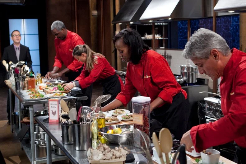Chopped Host Ted Allen watching celebrities: Charles Oakley, Brandi Chastain, Jackie Joyner-Kersee and Greg Louganis finish working on their appetizers that must include: Organic green juice, alligator, hen of the woods mushroom and mini rainbow marshmallows, as seen on Food Network's Chopped, Season 19.