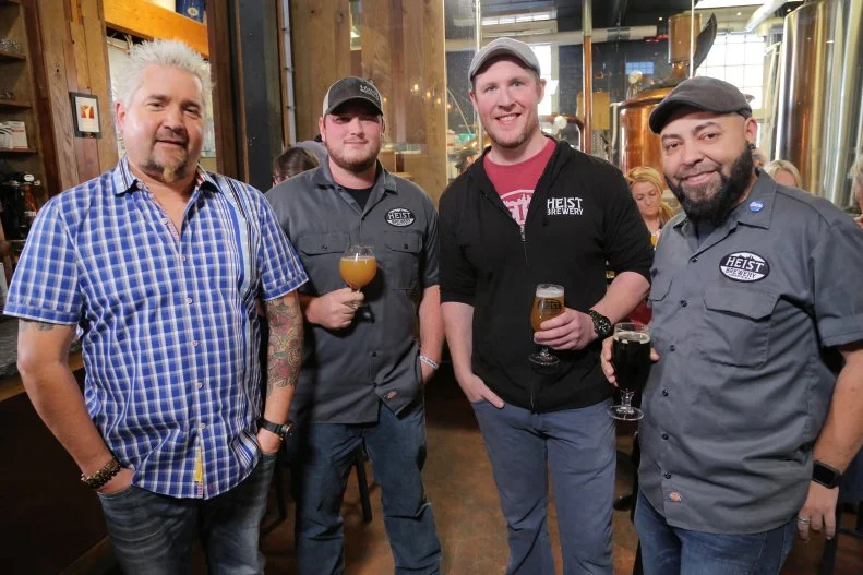 Host Guy Fieri posing with Buisness Partners Spencer Farrell, Kurt Hogan, and Eric Mitchell at Heist Brewery in Charlotte, North Carolina, as seen on Food Network's Diners, Drive-Ins and Dives, Episode 2608.