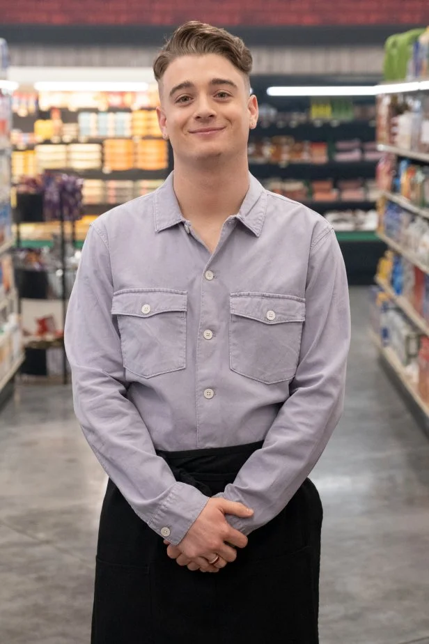 Contestant Jules Fieri, as seen on Guy's Grocery Games, season 31, standing in a supermarket aisle.