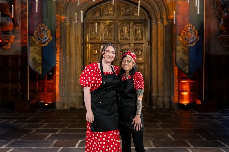 Contestants Sarah Arnold and Marjorie Santaromana pose in The Great Hall on the Harry Potter: Wizards of Baking, Season 2 set, as seen on Harry Potter: Wizards of Baking, Season 2.