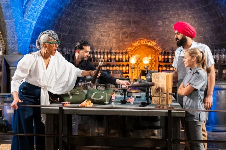 Judge Carla Hall and Judge Jozef Youssef with contestants Jujhar Mann and Katie Bonzer’s replicated showpieces White heart potion and Butts of Bat, a Ginger Whack Bonbon during judging, as seen on Harry Potter: Wizards of Baking, Season 2.