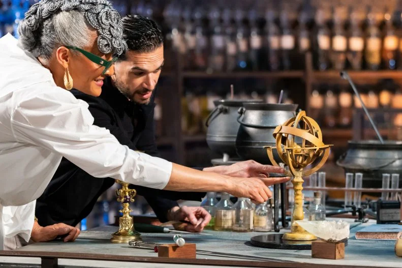 Judge Carla Hall and Judge Jozef Youssef with contestants Jenny Chambers and Alex Madrigal’s replicated showpieces Bowl of lemon sweets, a Sherbet Memory Cake and small sphere, Hidden Spell Bon Bon during judging, as seen on Harry Potter: Wizards of Baking, Season 2.