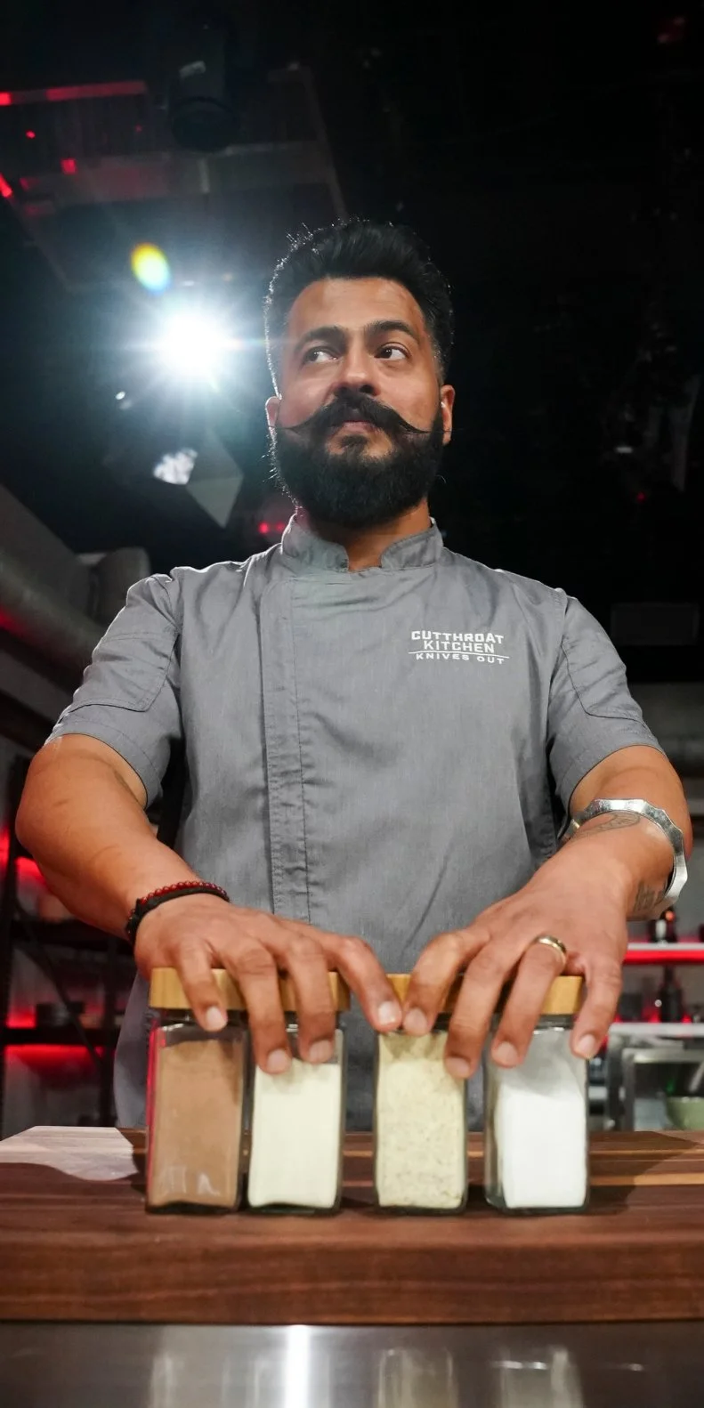 Chef Saransh Oberoi standing with his spices, as seen on Cutthroat Kitchen: Knives Out, Season 1.