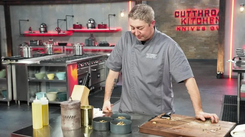 Chef Stephen Coe standing at station with plated dishes, as seen on Cutthroat Kitchen: Knives Out, Season 1.