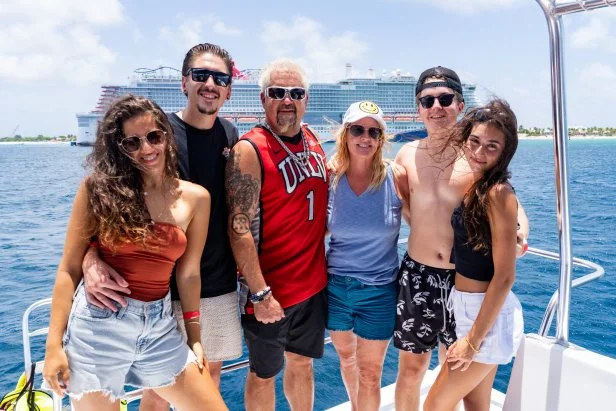 Food Network host Guy Fieri, Tara Bernstein, Hunter Fieri, Lori Fieri, Ryder Fieri, and Sophia Mrad standing on the deck of a ship as seen on Guy's Ultimate Family Cruise, Special 1.