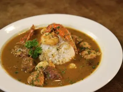 A bowl of gumbo with shrimp, crab and sausage with rice and topped with parsley in a white bowl.