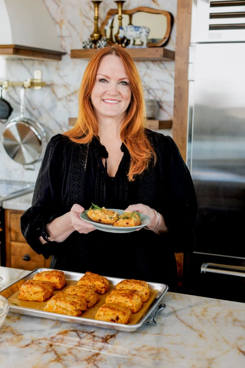 Ree Drummond, Food Network's Pioneer Woman, holding a plate of Pimento Cheese Biscuits with Sweet Spicy Butter at a kitchen counter
