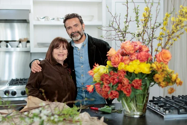 Though Ina is the undeniable mistress of delicious, seemingly effortless cooking, and has planned a delicious menu of a berry studded ricotta cake for breakfast followed by a decadent lunch of smash burgers and champagne, Daniel has some skill sharing of his own to do. He arrives at Ina's East Hampton home with a sumptuous bouquet of flowers for his hostess. Gathering up his bundle of brown paper wrapped flowers, Daniel uses a pair of garden shears and begins to show Ina some of the tips and tricks of flower arranging. First, he separates each type of flower into its own pile before filling a large glass vase with individual bundles of richly colored coral, yellow and pink flowers, to give the feeling of a flower garden with layers of color. “I really try to avoid anything that feels like filler,” says Daniel. As a final touch in the back of the glorious explosion of color, Daniel adds quince branches with tiny white flowers and the vibrant yellow of forsythia branches. “I’m just gobsmacked! I can’t believe how gorgeous this is,” beams Ina.
