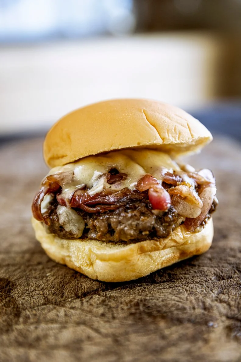 Twenty-percent fat and 80 percent lean is Ina’s magic formula for a great hamburger base. Next, ground mustard, salt, pepper and the real work begins: kneading the dry ingredients into the meat. “Isn’t a chef’s best tool his hands?” Daniel grins.

“The key to this is don’t press it together, just keep it light,” guides Ina.

“And fluffy,” adds Daniel.

Fun fact: Ina never served burgers at the Barefoot Contessa Fine Foods market in – because it was a takeaway destination rather than a place where food was made to eat there.

What does Ina do to unwind after she wraps up a cookbook Daniel wants to know.
Paris, of course. “I just know I’m going to relax there, I’m going to chill out, and I’m going to disconnect.”

 Though their perception of Paris may be different. It’s work for Daniel, and play for Ina, they do have one big thing in common notes Daniel. When they’re on, they’re really on and when they’re not? “You and I have two speeds,” says Daniel.

Ina agrees: “110 miles an hour and fast asleep,” she laughs.

“The trick is, I freeze them for 15 minutes and it just keeps the inside from overcooking,” says Ina. For a lady who knows her way around a burger Ina says it’s not a food she makes very often.

Next step: sauteeing two red onions. Ina prefers their slightly more sweet flavor. She cooks them at a very low temperature for about 10 minutes and adds sugar. Then it’s time to make the burgers: Ina advises smashing them down with a large metal spatula to form a crust on the burger. Cook them for a minute and a half on one side and then turn them over.

The Theater of the Runway, the Theater of Barefoot Contessa
There are some similarities to their passions, Ina muses. “I always think of whatever I did at Barefoot Contessa as theater,” says Ina.

“You get 500 people in one space you get them for 15 minutes and so you have to hit them where it hurts, and the way to do that is with music.”

Daniel is prompted to add a tablespoon of vinegar to the onions to finish them off. “What that does is scrapes up all the little crusty bits and deglazes the pan,” says Ina.
