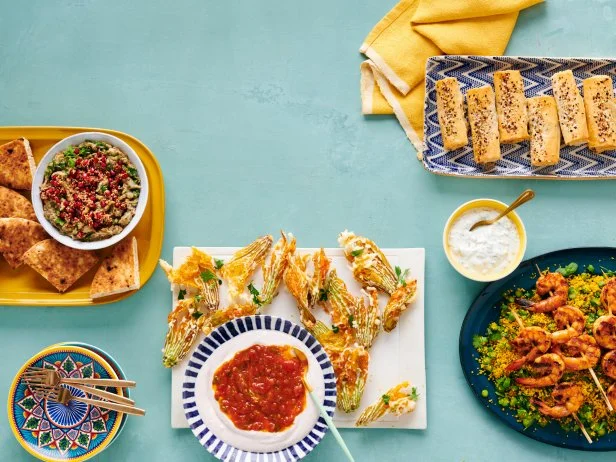 Counterclockwise from left: Babaganoush with Pomegranate Seeds, Crispy Squash Blossoms with Tomato Jam and Whipped Goat Cheese, Spiced Shrimp with Couscous and Preserved Lemon Yogurt, and Phyllo Cigars with Ricotta and Feta.