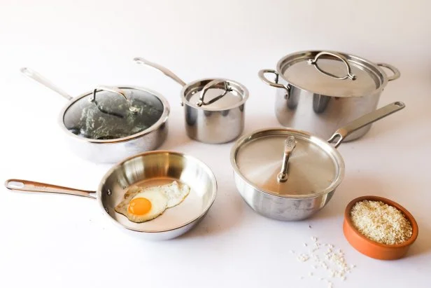 Five pieces of stainless steel cookware arranged on a white countertop