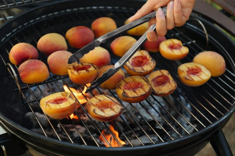 Woman cooking tasty peaches on grill, closeup