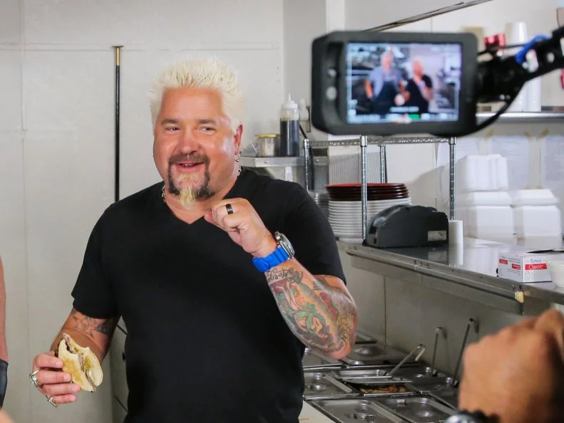 Guy Fieri smiling as he samples the filet mignon sandwich as prepared by Chef/Owner Ed Ferencik during his original DDD vistit to Butcher's Kitchen Char-B-Que in Reno, Nevada, as seen on Food Network's Triple D Nation, season 8.
