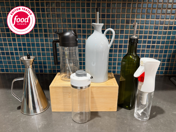 Six olive oil dispenser bottles arranged on a concrete countertop and wooden block