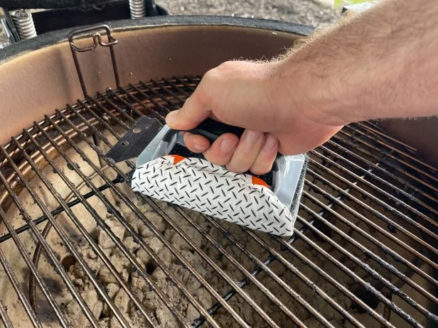 The Proud Grill Q-Swiper Grill Cleaner Set being used to clean a kettle charcoal grill's grates