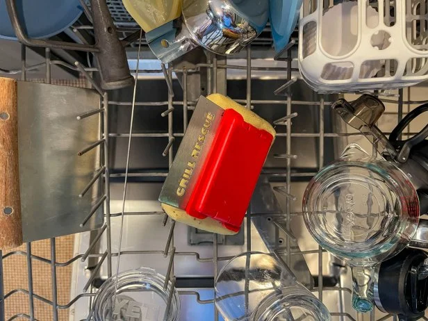 Scrubbing pad of the Grill Rescue grill brush on a dishwasher rack with other dishes and kitchen tools