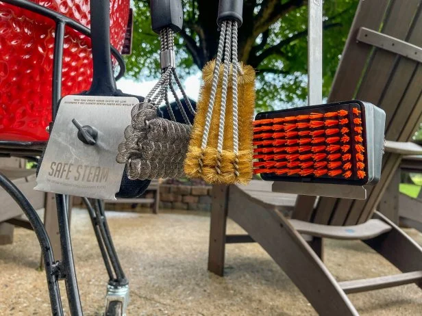 Williams Sonoma, Kona, Grillaholics and Oklahoma Joe's grill brushes hanging off a kamado grill on a stone patio