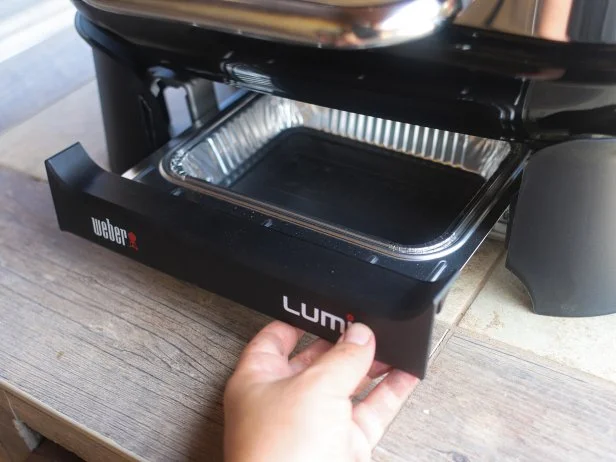 A hand pulling out a grease tray underneath the Weber Lumin electric grill