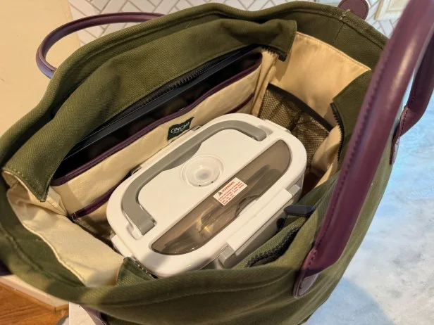 Top view of a white electric lunchbox inside an olive green and beige work tote