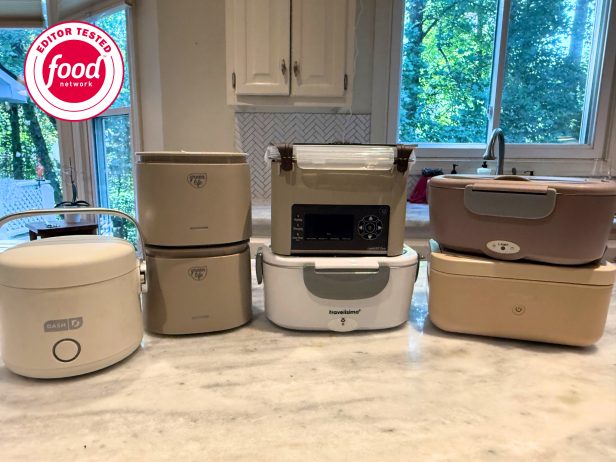 Seven electric lunchboxes in neautral colors arranged together on a white marble countertop in a white kitchen