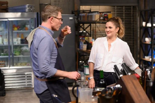 Bobby Flay nhấp một ngụm rượu bourbon trong khi Drew Barrymore đến thăm khu vực nấu ăn của anh ấy.