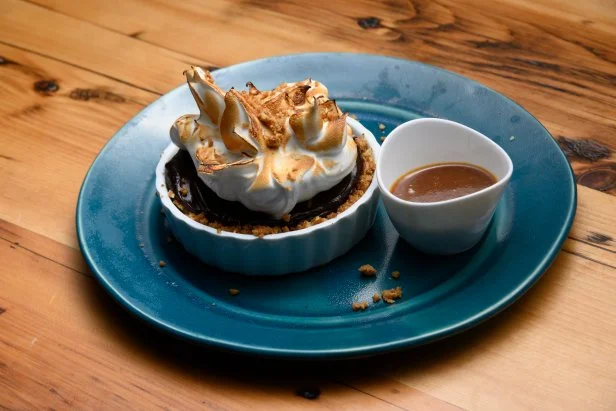 A small chocolate cream pie topped with toasted meringue and a side of caramel.