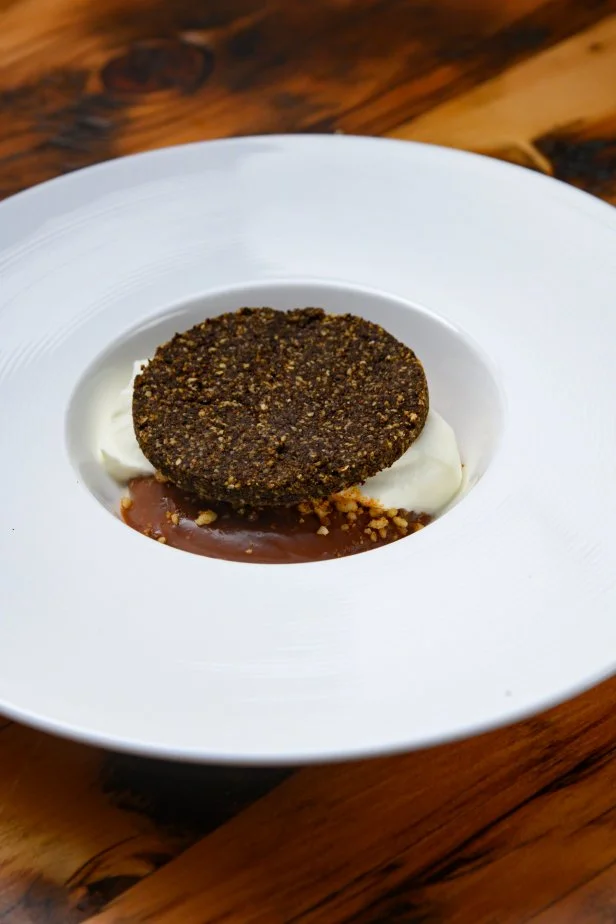 A disc of crust tops an upside-down chocolate cream pie, atop chocolate pudding a dollop of whipped cream.