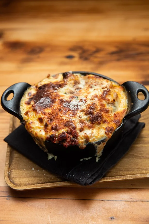 Pastitsio dish in a double handled cast iron dish on a wood cutting board.