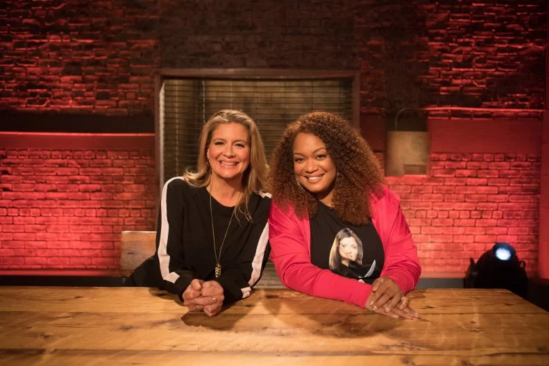 Co-hosts Amanda Freitag and Sunny Anderson pose at the table, as seen on Beat Bobby Flay, Season 27.