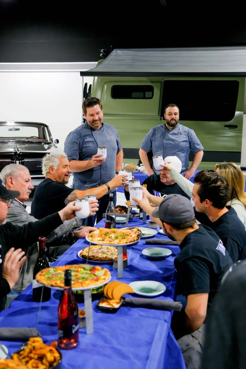 Host Guy Fieri and guests enjoy a meal prepared by Chef Dustin Valette inside VP Speed Shop, a 25,000 square foot state-of-the-art vintage car showroom and custom hot rod shop, located in Santa Rosa, CA, as seen on Diners, Drive-In's and Dives: Revved Up.